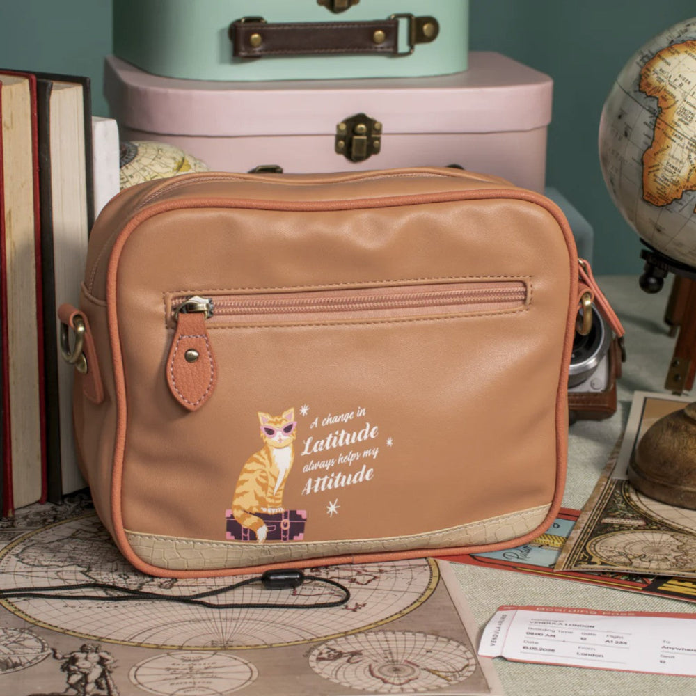 Brown travel bag with a cat illustration and text, placed on a map with vintage books and a globe in the background.