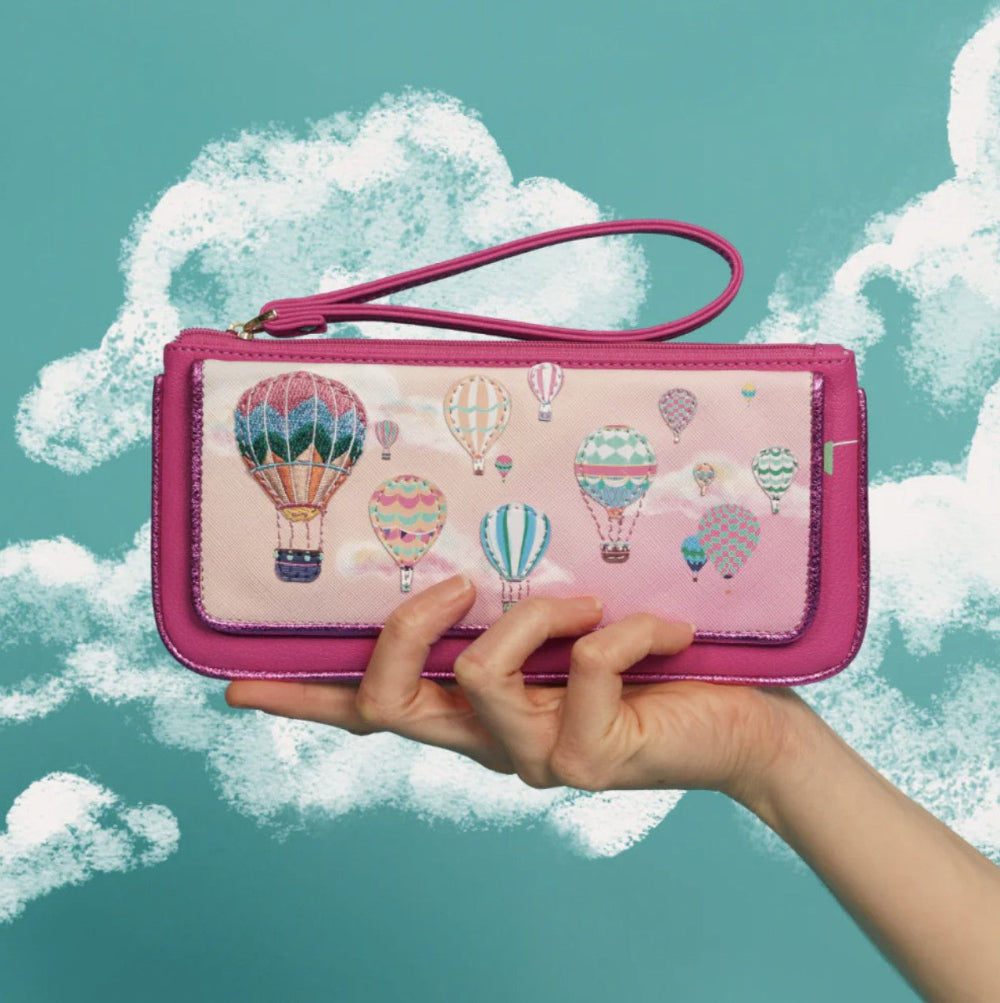 Pink wallet with hot air balloon design held by a hand against a cloud background