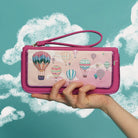 Pink wallet with hot air balloon design held by a hand against a cloud background
