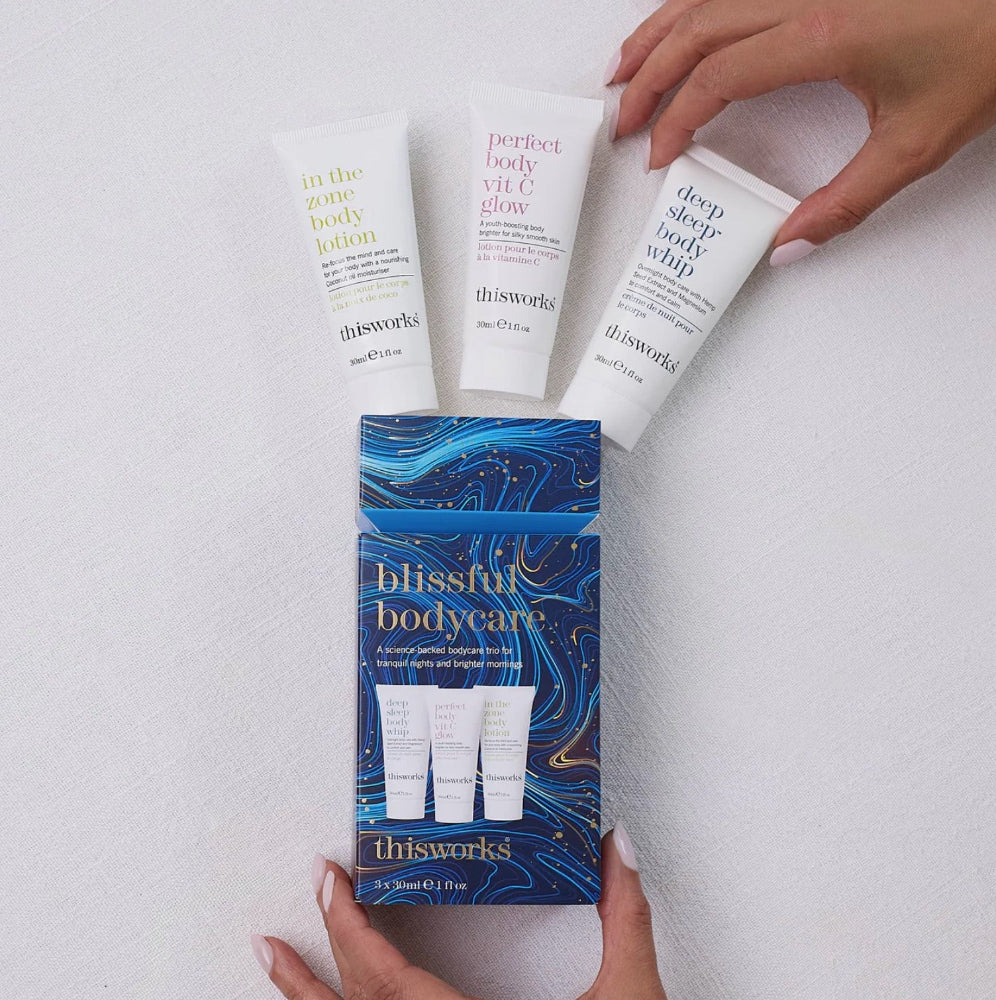 Three tubes of 'this works' body care products with a box labeled 'blissful bodycare' on a light gray background.