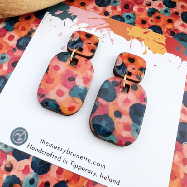 Colorful abstract-patterned earrings on a branded card with a colorful background