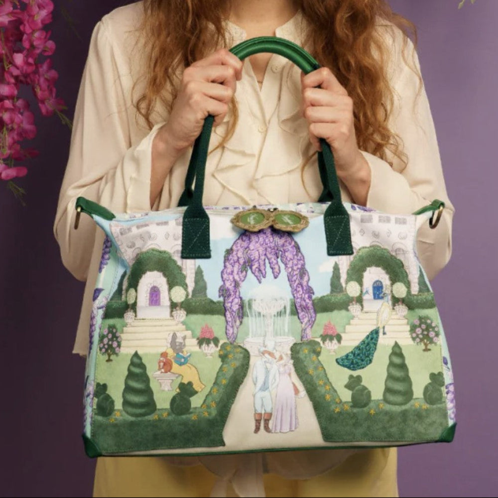 Person holding a large, colorful tote bag with a garden scene design against a purple background with flowers.