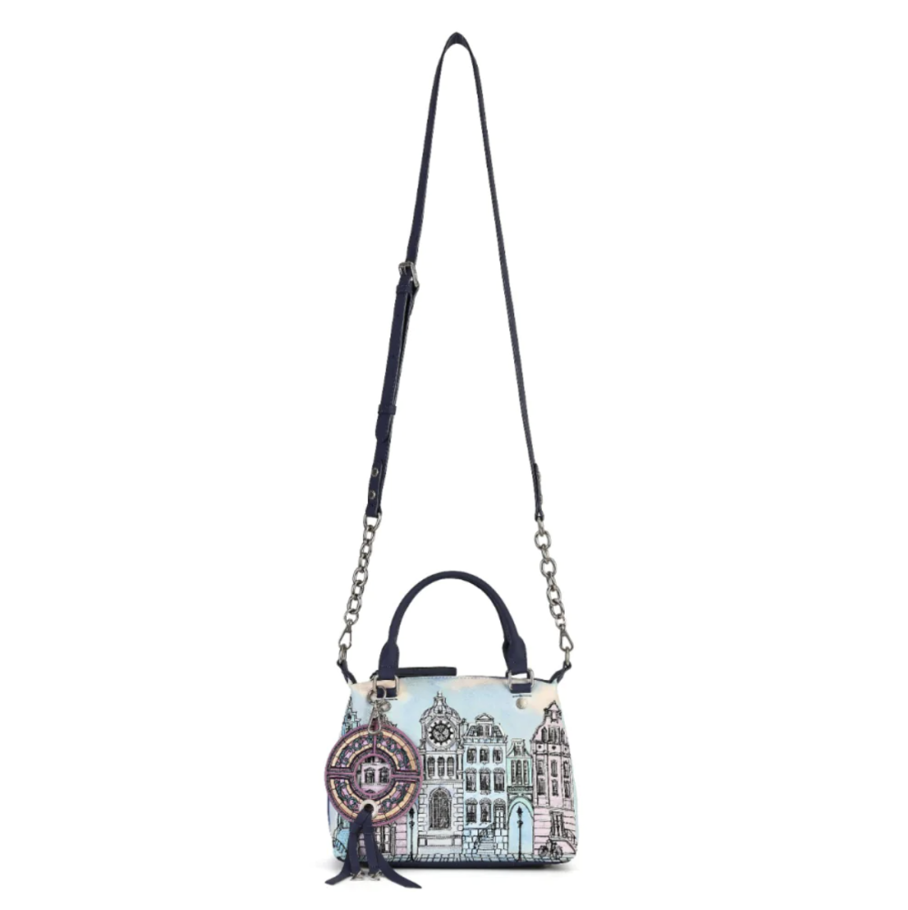 A small structured handbag with a navy leather top handle and shoulder strap, featuring a light blue and white architectural illustration print and a circular hanging charm, shown on a plain white background.