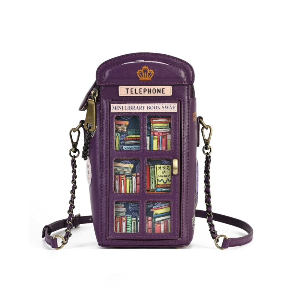 A purple faux-leather crossbody phone bag designed to look like a telephone booth, featuring a gold crown logo, a 'TELEPHONE' sign, and a 'MINI LIBRARY BOOK SWAP' label. The front has six illustrated bookshelves filled with colorful books, and the bag is shown with its black chain strap on a white background.