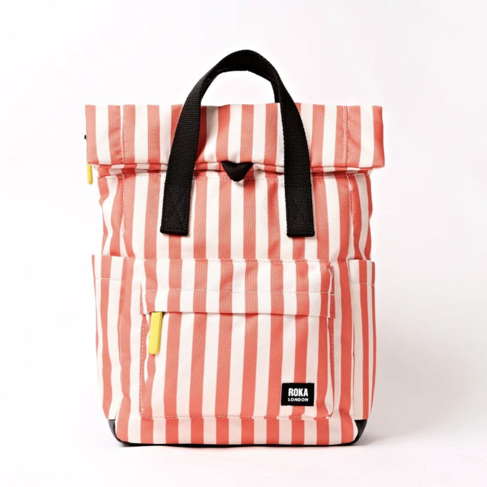 A striped roll-top backpack in pink and white with black handles and a small black ROKA label on the front pocket