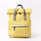 A yellow ROKA London roll-top backpack with grey handles and a grey reflective stripe on the front zip pocket.