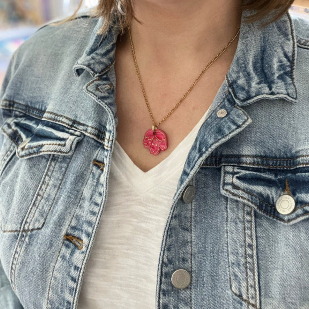 Person wearing a denim jacket with a necklace featuring a pink heart pendant.