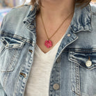 Person wearing a denim jacket with a necklace featuring a pink heart pendant.