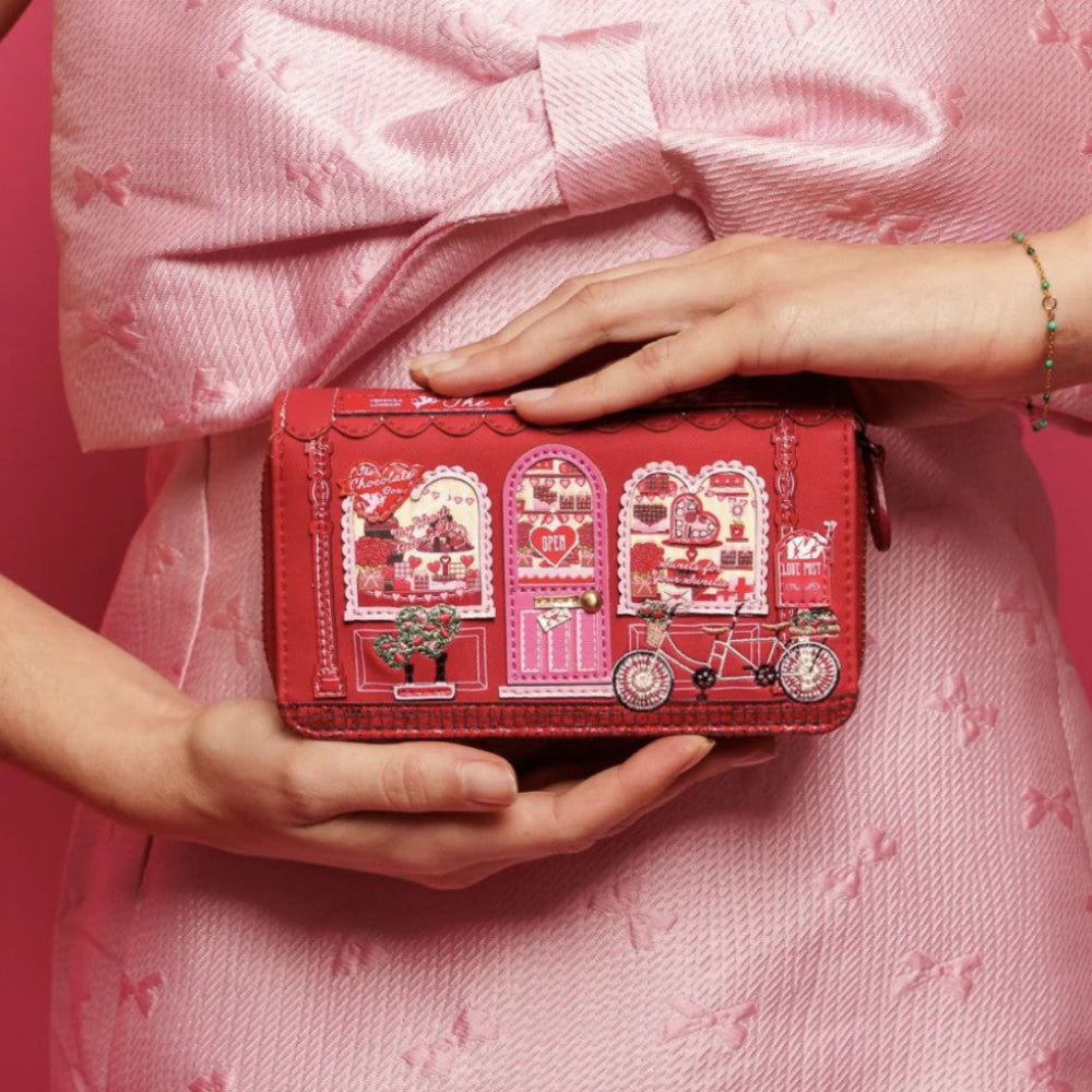 Person holding a red patterned wallet against a pink background