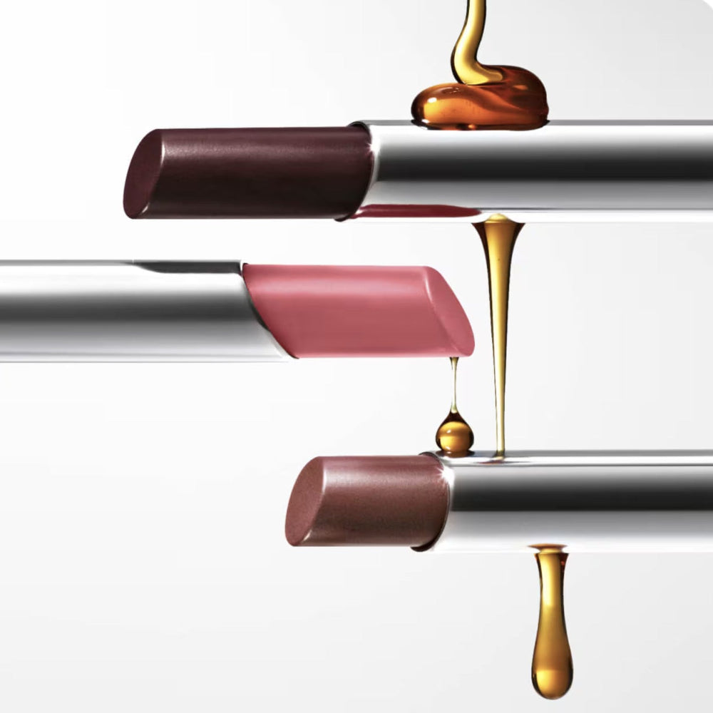 Three lip glosses with gold liquid droplets on a white background