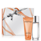 Clinique Happy gift set featuring a white and orange gift box with a silver ribbon, an orange body cream tube, and a clear glass fragrance bottle with a silver cap on a white background.