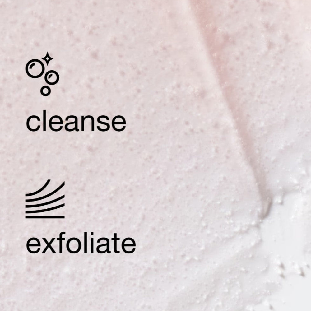 Close-up of a pale pink exfoliating cleanser with visible foam bubbles and black text reading 'cleanse' and 'exfoliate' on a light pink textured surface.