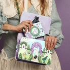 Person holding two colorful bags with garden-themed designs against a purple background