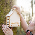Person holding a wooden bee hotel against a tree