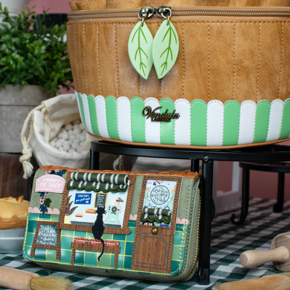 Handbag with a detailed design featuring a cat and various elements, placed on a checkered tablecloth.