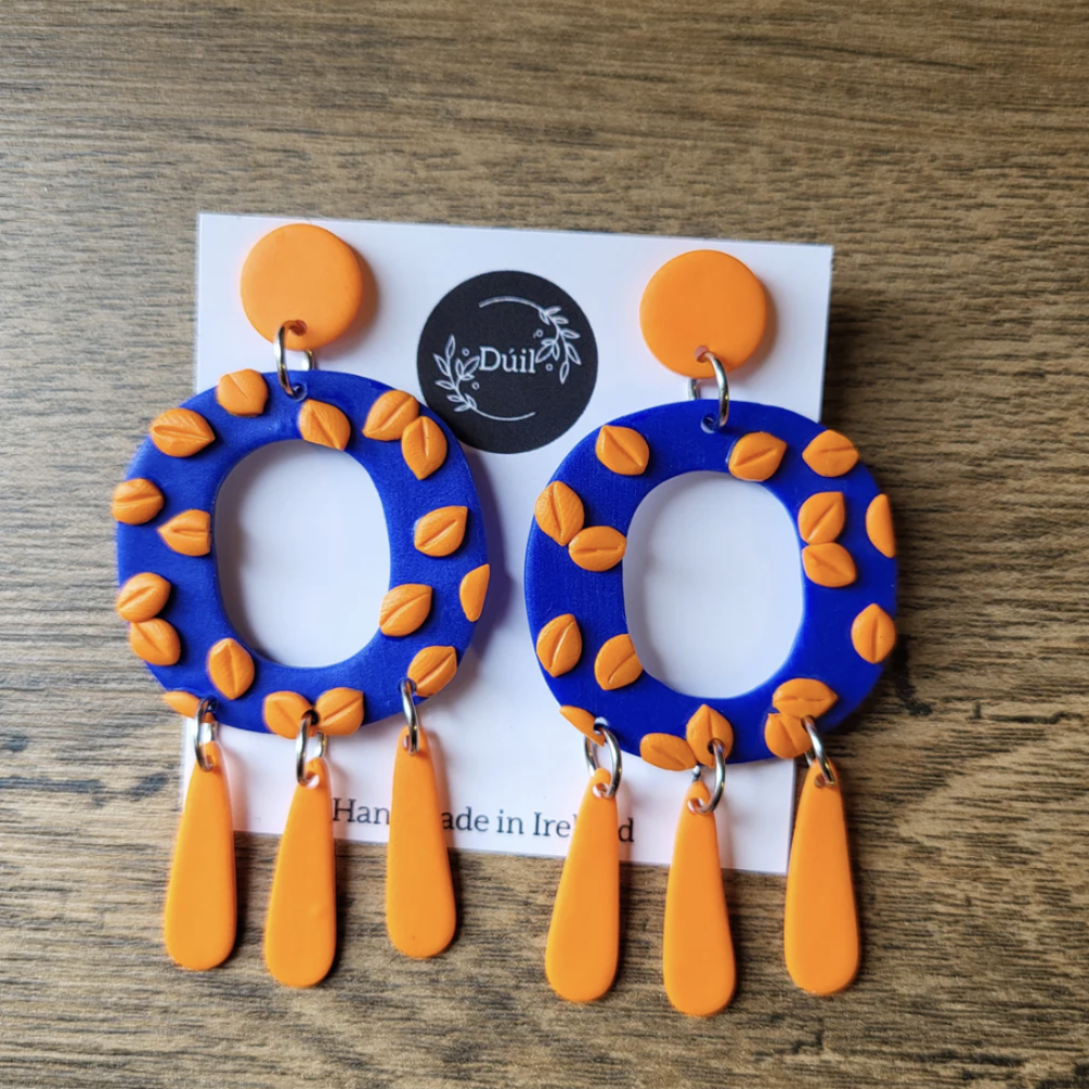Blue and orange earrings on a display card with 'Duil' branding on a wooden surface.