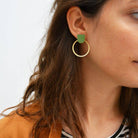 Close-up of a person wearing gold hoop earrings with green heart charms.
