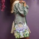Person holding a colorful handbag with floral design against a purple background