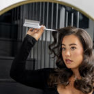 Woman with styled hair holding a comb in front of a mirror