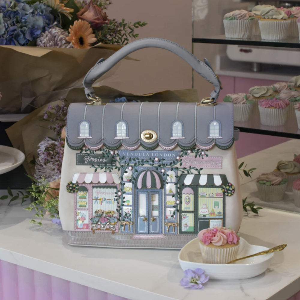 Handbag with a decorative design of shops on a table with cupcakes and flowers.