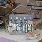 Handbag with a decorative design of shops on a table with cupcakes and flowers.