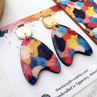 Colorful butterfly-shaped earrings on a branded card with 'the messy brunette' logo.