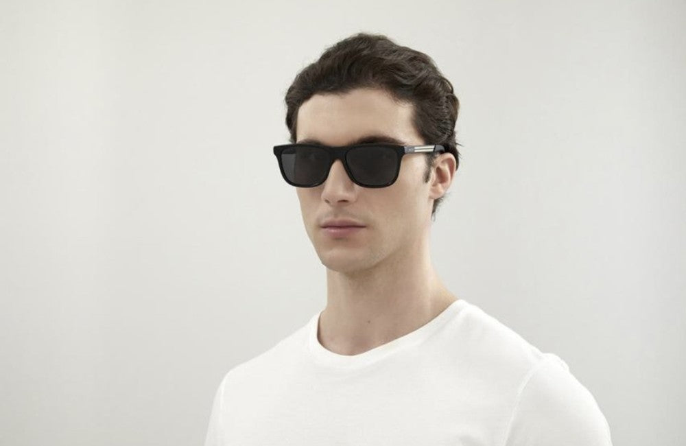 Man wearing black sunglasses and a white shirt against a plain background