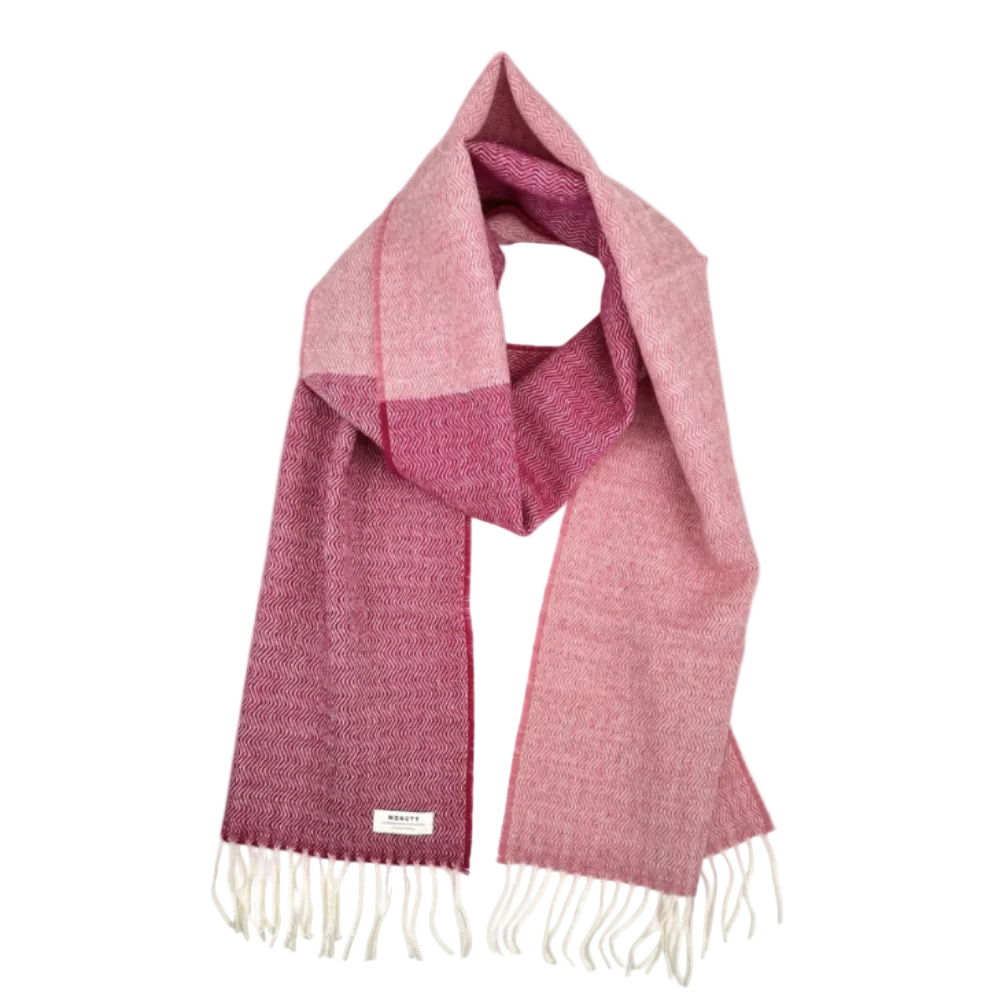 A woven scarf with a color-blocked pattern in shades of dusty pink and magenta, finished with cream-colored fringe and a small white brand label.