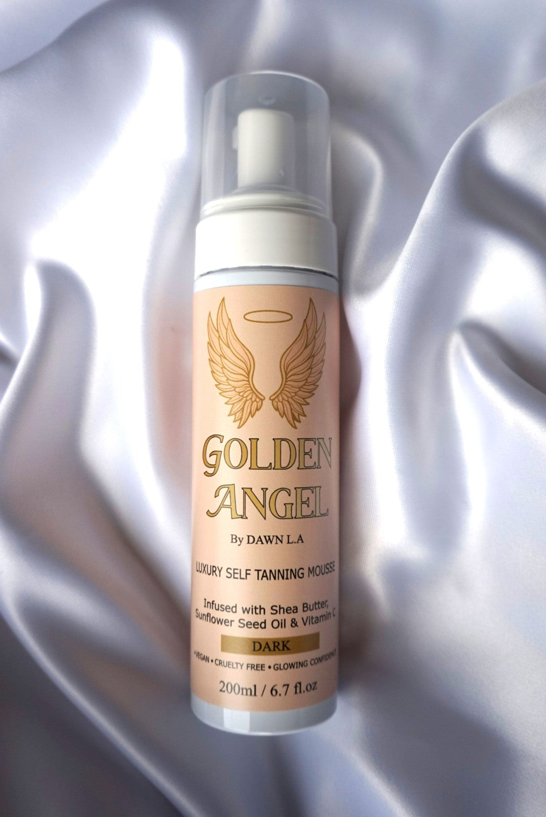 A bottle of Golden Angel Luxury Self Tanning Mousse in the 'Dark' shade, displayed on a draped white satin fabric background.