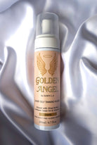 A bottle of Golden Angel Luxury Self Tanning Mousse in the 'Dark' shade, displayed on a draped white satin fabric background.