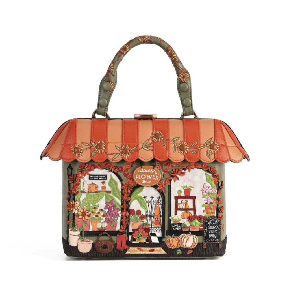 A decorative handbag designed to look like a storefront, featuring a scalloped orange and peach awning with floral embroidery, a top handle, and a detailed autumn-themed facade with pumpkins, flowers, and a chalkboard sign.