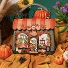 A decorative handbag styled in an autumn scene with pumpkins, flowers, and draped orange fabric. The bag has a scalloped orange top, a green body, and a detailed illustrated storefront design on the front with autumn-themed embellishments.
