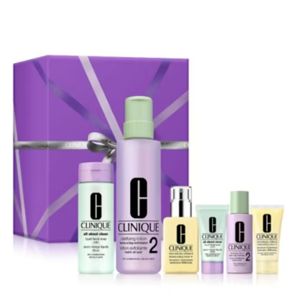 Clinique skincare gift set featuring a purple gift box with a silver ribbon and six cosmetic bottles and tubes in pastel shades, arranged on a white background.