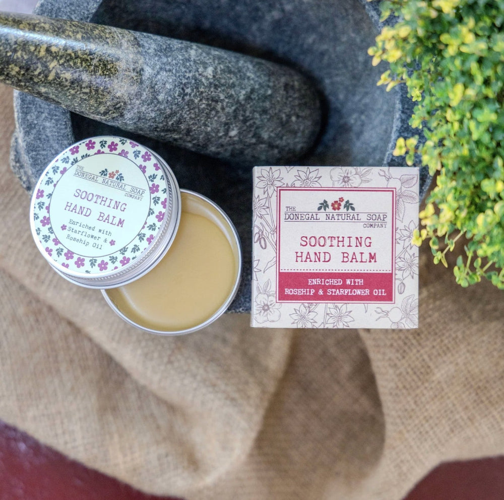 Soothing hand balm with packaging on a natural stone surface with plants.