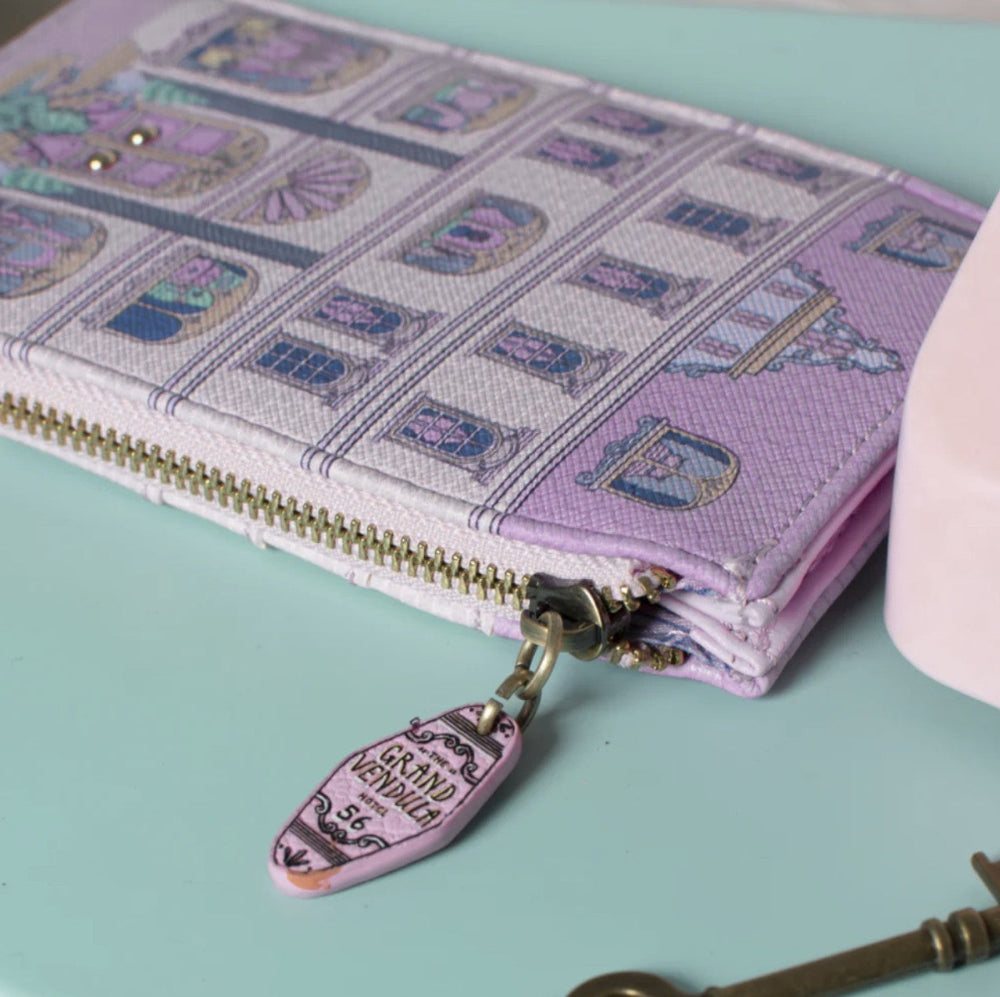 Pink wallet with decorative pattern and charm on a light blue background