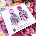 Pair of floral earrings on a display card with pink flowers in the background