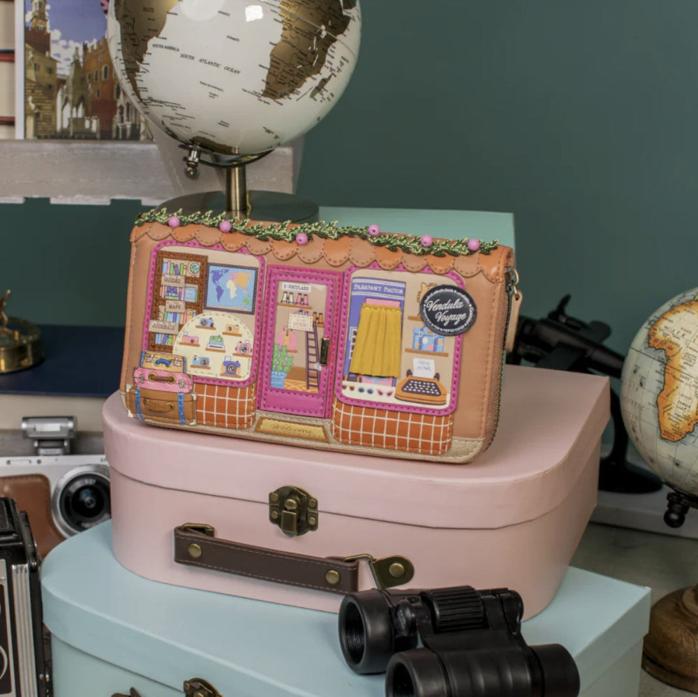 Decorative suitcase with travel-themed design on a surface with globes and binoculars.
