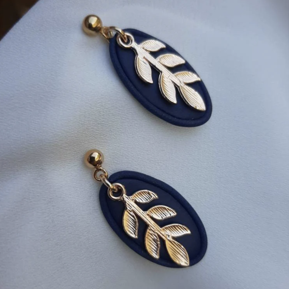 Pair of earrings with blue oval and gold leaf design on a light gray background