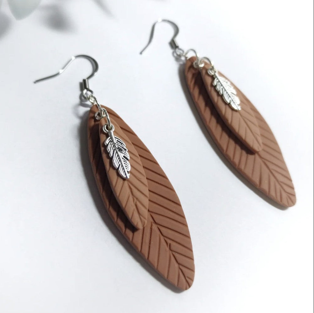 Brown feather-shaped earrings with silver details on a white background