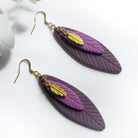 Purple feather-shaped earrings with gold accents on a white background