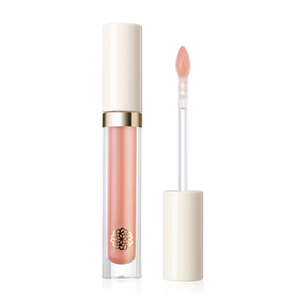 A clear tube of liquid lip gloss with a pale peach-pink shade, shown next to its applicator wand with a matching nude-pink tip. The product features a glossy white cap, a gold metallic band, and a small gold logo near the bottom, set against a clean white background.