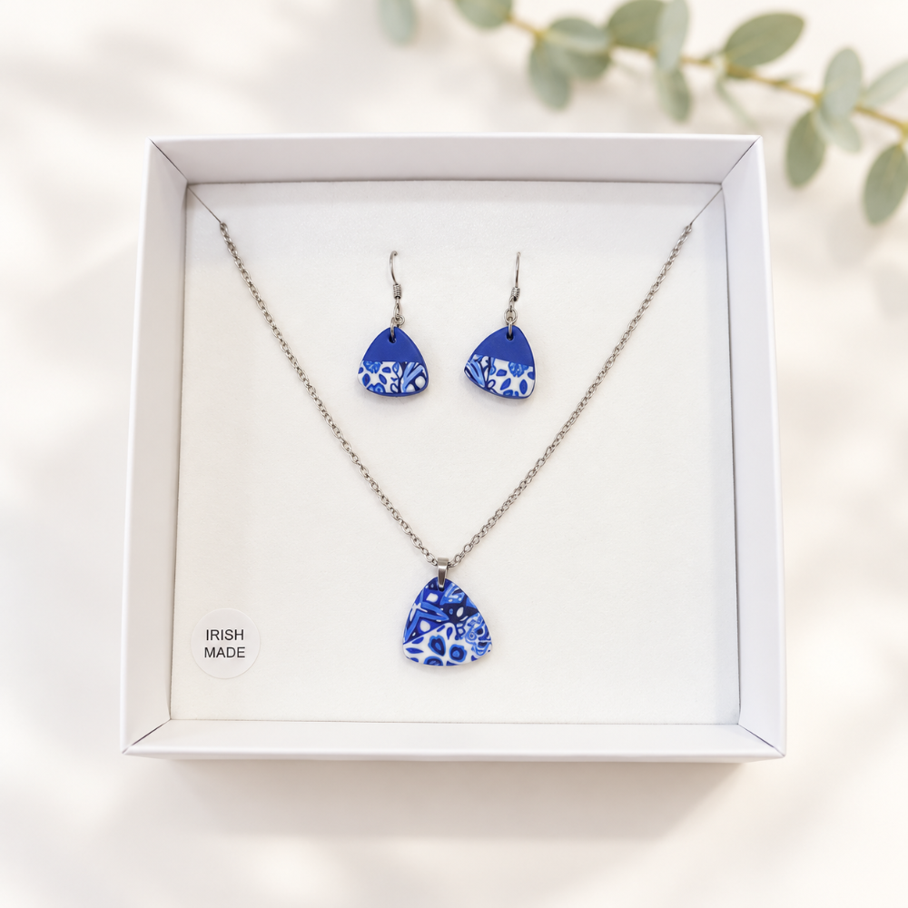 A jewellery set featuring a silver-tone necklace and matching drop earrings with blue and white floral patterned teardrop pendants, presented in a white gift box with 'IRISH MADE' printed on the inside.