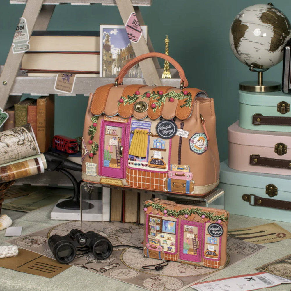 Decorative handbag with travel-themed design on a desk with books and a globe.