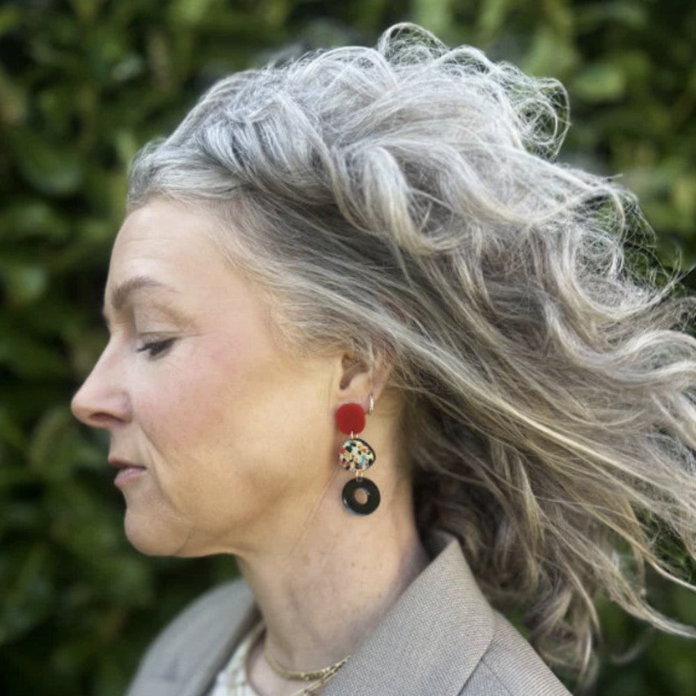 Woman with gray hair wearing colorful earrings against a green background