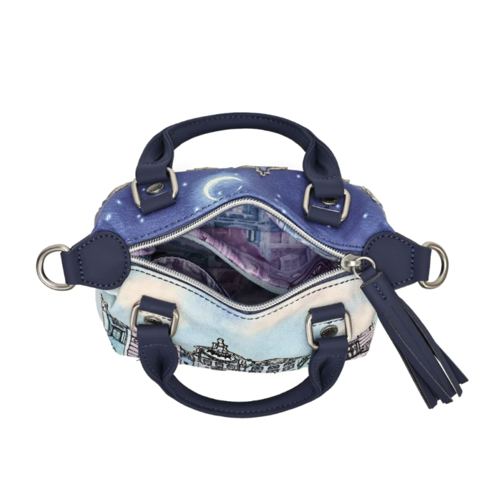 A small structured handbag shown open against a plain white background. The exterior features a blue and purple celestial print with a cityscape illustration near the bottom, navy blue leather handles and trim, silver-tone hardware, and a navy tassel charm.