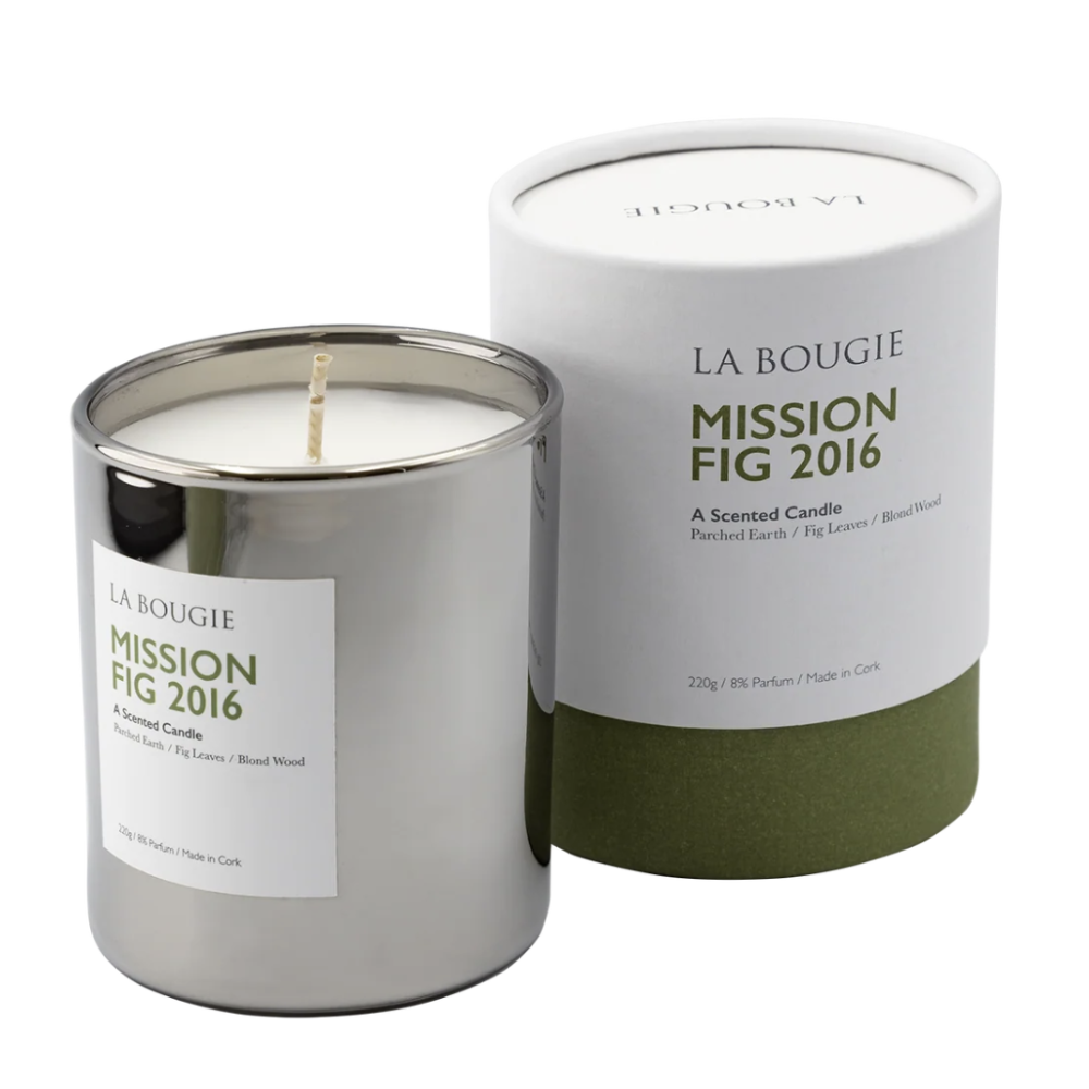 A La Bougie Mission Fig 2016 scented candle in a brushed silver metal tin with a white label, shown next to its white cylindrical cardboard packaging with an olive green base on a white background.