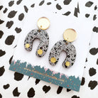 Pair of patterned earrings on a branded card with a black and white background