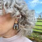 Close-up of a person with curly gray hair wearing a gold earring with a horseshoe design outdoors.