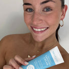 Woman holding a tube of Moogoo tanning cream against a plain background