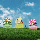 Three Daisy Marc Jacobs perfume bottles with colorful flower designs on a grassy field with a blue sky.